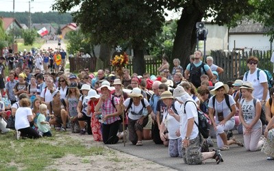 Pielgrzymi piesi z Płocka na Jasną Górę: jedna grupa przyklęka przed kościołem, kolejna zbliża się do miejscowości w parafii św. Benedykta w Płocku Radziwiu